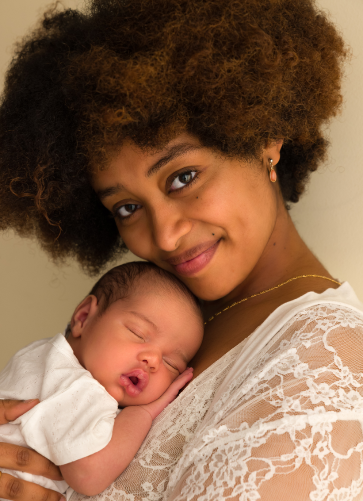 woman in white holding sleeping baby on her chest looking at the camera